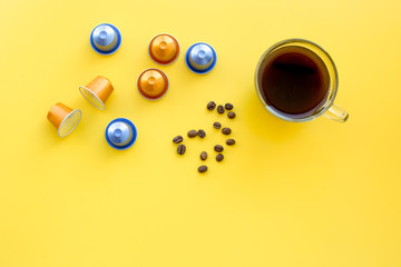 Beverage capsules for coffee mashine near coffee cup and grains on yellow background top view copyspace