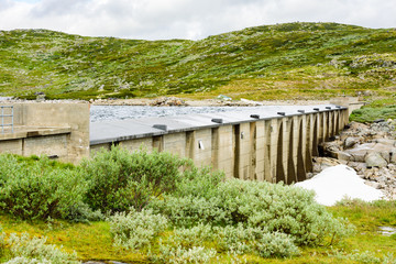 Filled water reservoir with small dam. Small pile of snow and ice below the concrete dam. Location Hardangervidda in Norway.