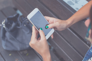 Woman hands using smartphone on a bench background in the park. Bali island, Indonesia.