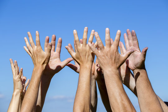 Group raising hands against blue sky background