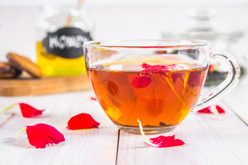 Floral black tea, honey can, petals on a white wooden table.