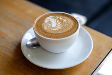 Cup of hot milk coffee with swan latte art on wooden table background. Concept of morning drink freshness. Selective focus
