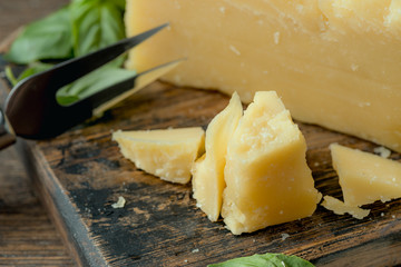 Parmesan cheese on wooden board with basil leaves. Pieces of cheese parmesan on wooden table and cheese fork.