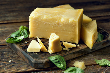 Parmesan cheese on wooden board with basil leaves. Pieces of cheese parmesan on wooden table.