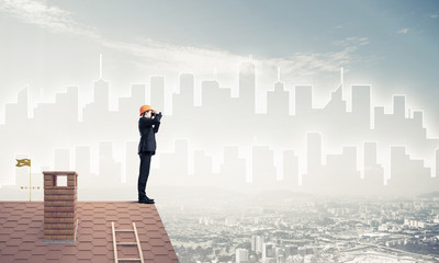 Engineer man standing on roof and looking in binoculars. Mixed m