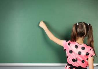 schoolgirl writing on empty blackboard, back view