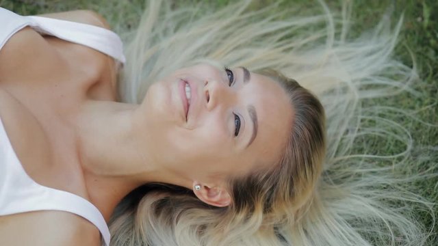 Beautiful woman relaxing lying on a grass in slow motion, attractive girl with beautiful hair enjoying a rest