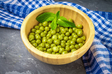 Canned peas in a wooden plate on a gray concrete background.