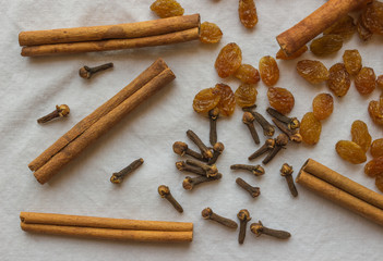 Dried cloves, cinnamon and raisins on a light fabric .