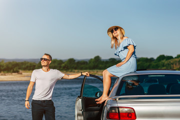 Happy traveler couple hugging a car by the river to the sunrise