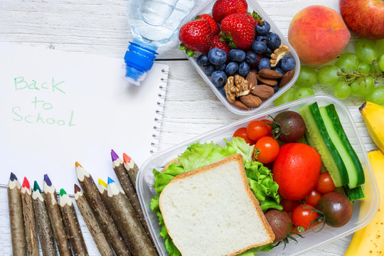 school lunch boxes with sandwich, fruits, vegetables and bottle of water with colored pencils and back to school inscription