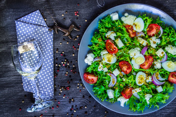 Salad of fresh vegetables and a glass of wine on a black wooden background.