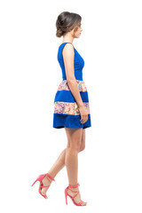 Side view of young woman in summer sleeveless blue short dress walking looking ahead. Full body length portrait isolated on white studio background.