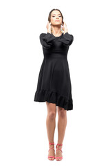 Vogue glamour woman in black dress touching hair with head tilted back pose.  Full body length portrait isolated on white studio background.