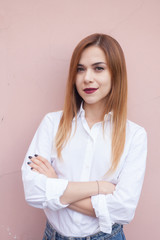 A woman stands at a bright wall in a white shirt and smiling