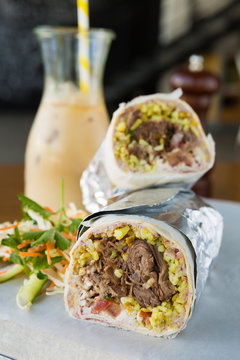 Mexican Shredded Beef Breakfast Burrito Sliced In Half Served With Ice Coffee.