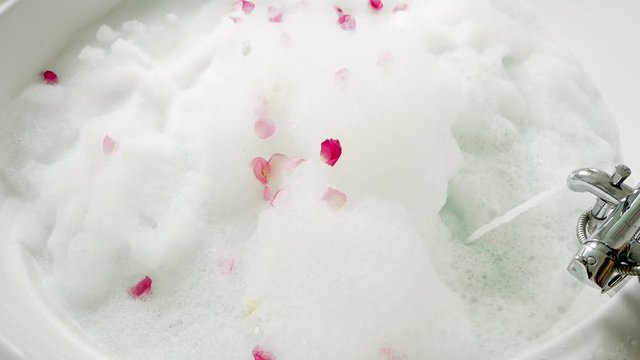 water flows from the tap in a bath with foam and rose petals