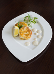 Beautiful fresh golden fish cakes, served with a wedge of lime, dill sauce and rocket on a white plate