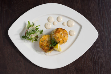 Beautiful fresh golden fish cakes, served with a wedge of lime, dill sauce and rocket on a white plate