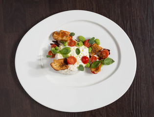 Delicious tomato and mozzarella cheese salad caprese, served on a white plate, with basil, croutons and balsamic vinegar.