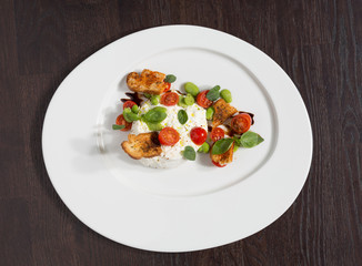 Delicious tomato and mozzarella cheese salad caprese, served on a white plate, with basil, croutons and balsamic vinegar.