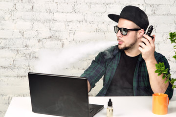 Young man sitting in office with a cup of coffee and vaping