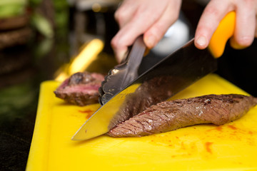 Cutting flame grilled, cooked kangaroo steak loin on a yellow cutting board