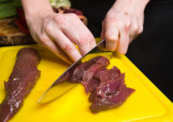Cutting fresh raw kangaroo steak loin on a yellow cutting board