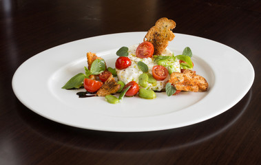 Delicious tomato and mozzarella cheese salad caprese, served on a white plate, with basil, croutons and balsamic vinegar.