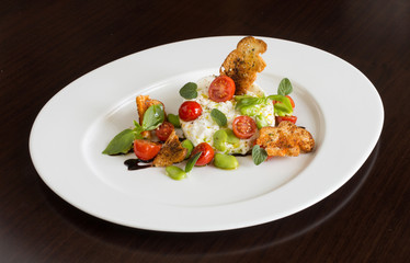 Delicious tomato and mozzarella cheese salad caprese, served on a white plate, with basil, croutons and balsamic vinegar.