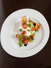 Delicious tomato and mozzarella cheese salad caprese, served on a white plate, with basil, croutons and balsamic vinegar.