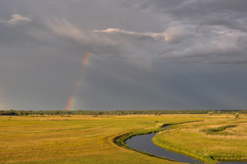 Rural landscape with river, field, trees after a thunderstorm. At sunset. Ukraine