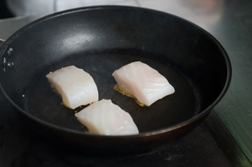 Pan fried golden fish fillet cubes, frying in real butter, in a non stick rustic pan.