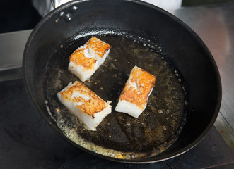 Pan fried golden fish fillet cubes, frying in real butter, in a non stick rustic pan.