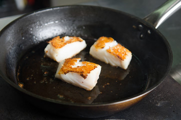 Pan fried golden fish fillet cubes, frying in real butter, in a non stick rustic pan.