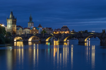 Fototapeta na wymiar Lit Charles Bridge (Karluv most) and old buildings at the Old Town and their reflections on the Vltava River in Prague, Czech Republic, at dusk.