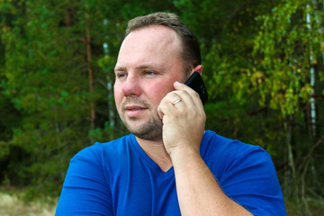 Man talking on mobile phone in nature, green background. Communication without borders and outside the city.The unshaven man.