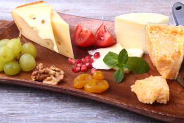 Assortment of cheese with fruits, grapes, nuts and cheese knife on a wooden serving tray.