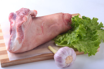 Raw pork knuckle, garlic and lettuce leaves on a cutting board. Selective focus. Ready for cooking.