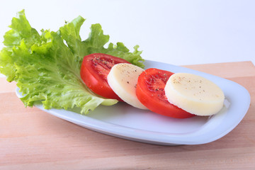 Portion of Mozzarella with Tomatoes, lettuce leaf and Balsamic dressing on white plate. selective focus close-up shot.