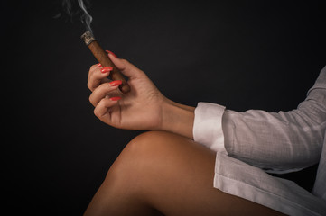 Closeup of woman hand holds cigar on her bare leg
