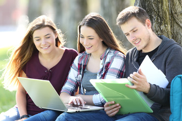 Three happy students studying online in a park