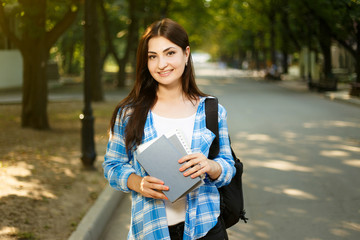 Summer holidays, education, campus and teenage concept. Smiling female student with books and backpack standing in park