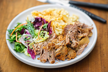 Pulled pork with mashed potatoes and mixed leaves salad on white plate 
