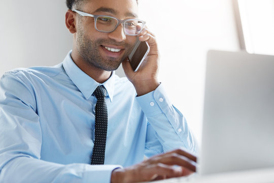 Young owner of company calling financial manager, having happy look in his notebook, being glad to see big profits of his company. Businessman signing new contract with his parter over mobile phone