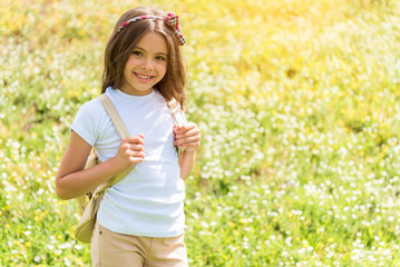 Joyful female kid walking on grassland with rucksack