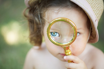 Portrait of a little pretty girl looking through magnifier