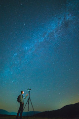 The man with a camera stand on the background of the starry sky. night time