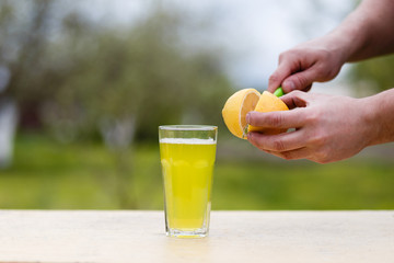 Energy drink into a glass on a wooden table. lemon cut with a knife shed. Side view of homemade lemonade cooking with yellow lemon and water in glass jar in wooden table.