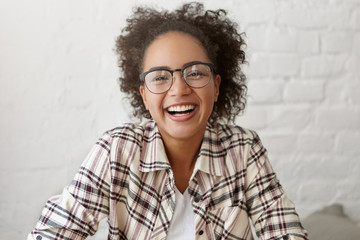 Happy female with dark pure skin and crisped hair wearing elegant glasses and shirt smiling...